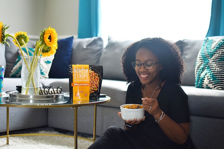 Black woman in living room with bowl of Vegan Southern Chicken and Rice