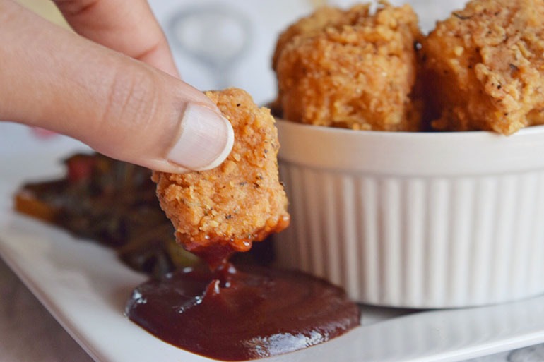 Hand holding Chicken Fried Tofu dipping into sauce