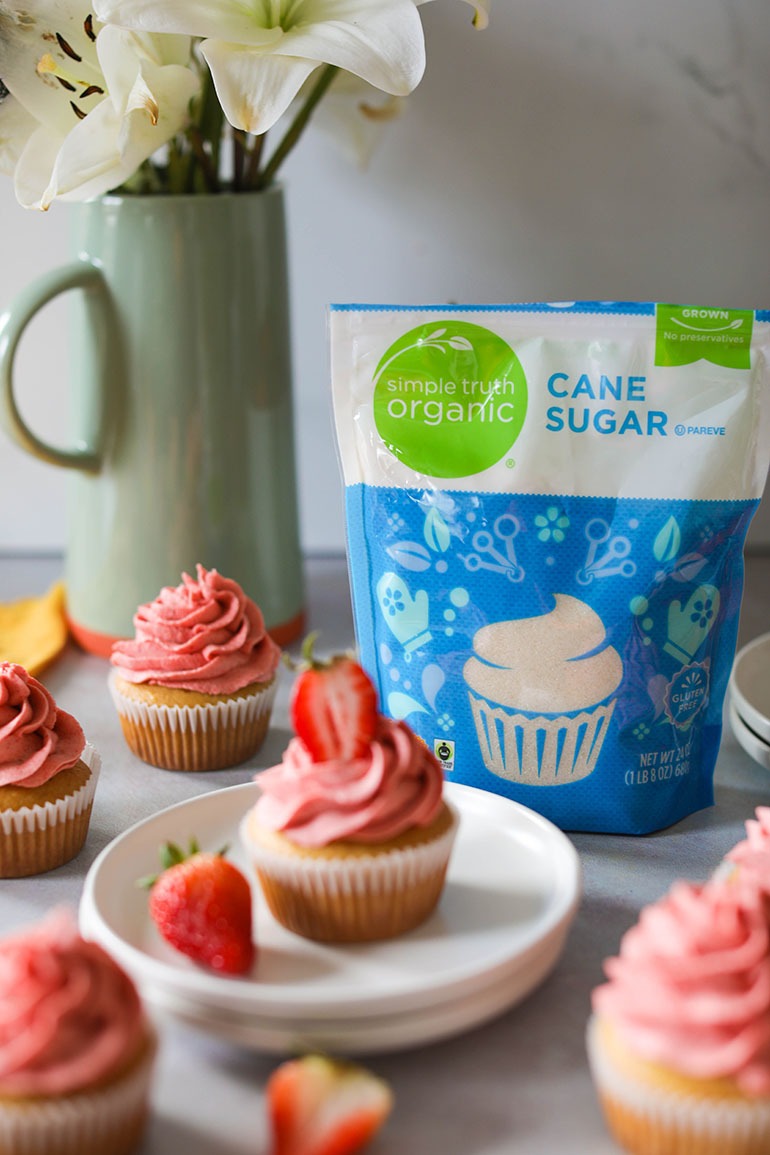 Vegan Strawberry Cupcakes on white plate with bag of sugar in focus