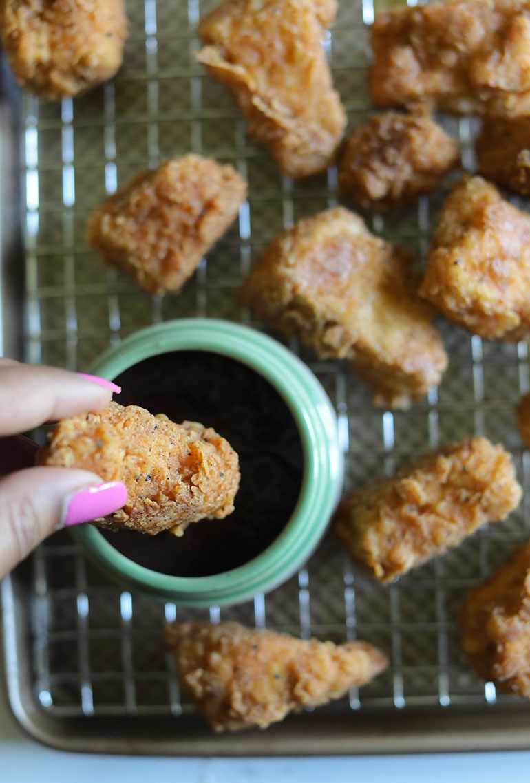 Spicy Chicken Fried Tofu on cooling rack with brown hand dipping