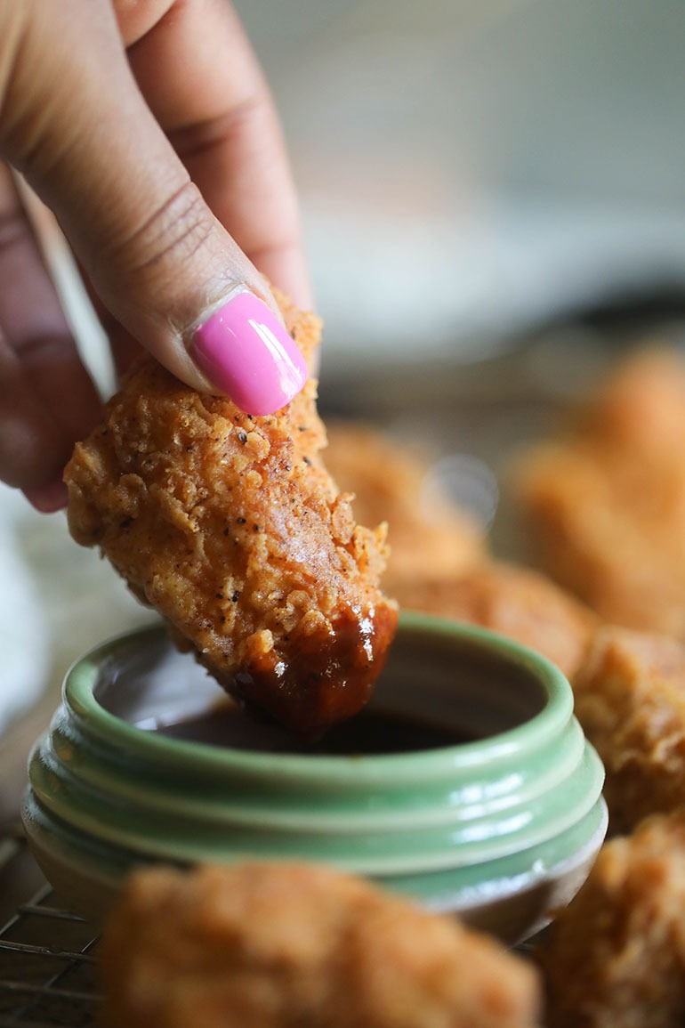 Brown hand dipping Spicy Chicken Fried Tofu in sauce